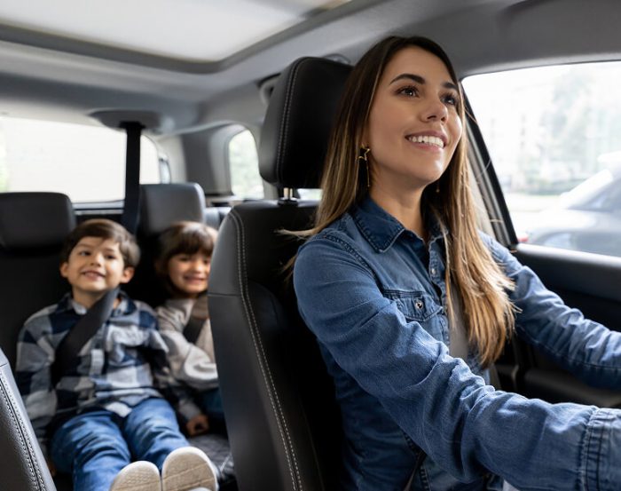 Lady with a nice smile driving her children sitting in the back of a car.